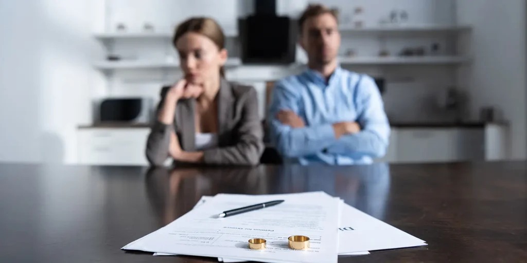 wedding rings on divorce papers with divorced couple blurred in the background. New divorce laws Uk 2023