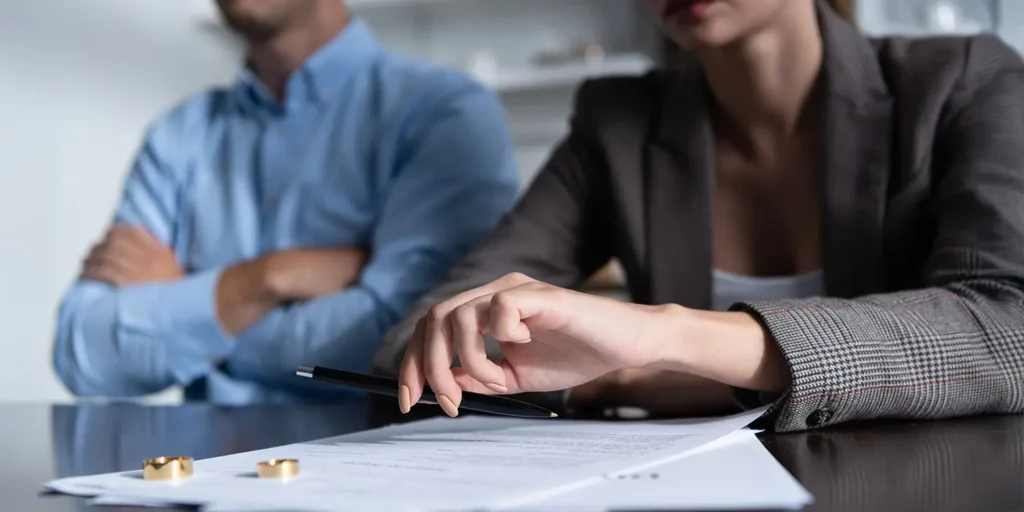 Two people signing divorce papers with rings on a table, symbolising the division of assets in UK divorce proceedings.