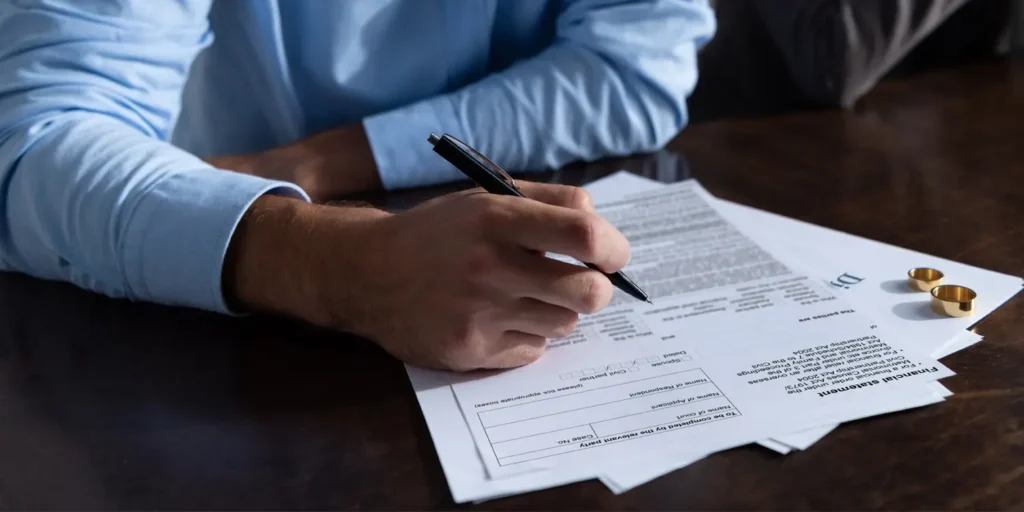 Person completing Form E financial statement with wedding rings on divorce papers