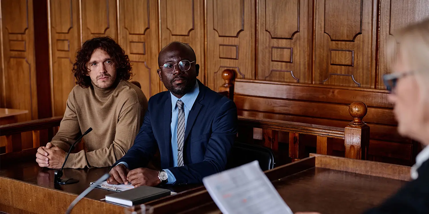 Two people sitting in a courtroom beside their solicitor during a legal hearing about a disputed Will.